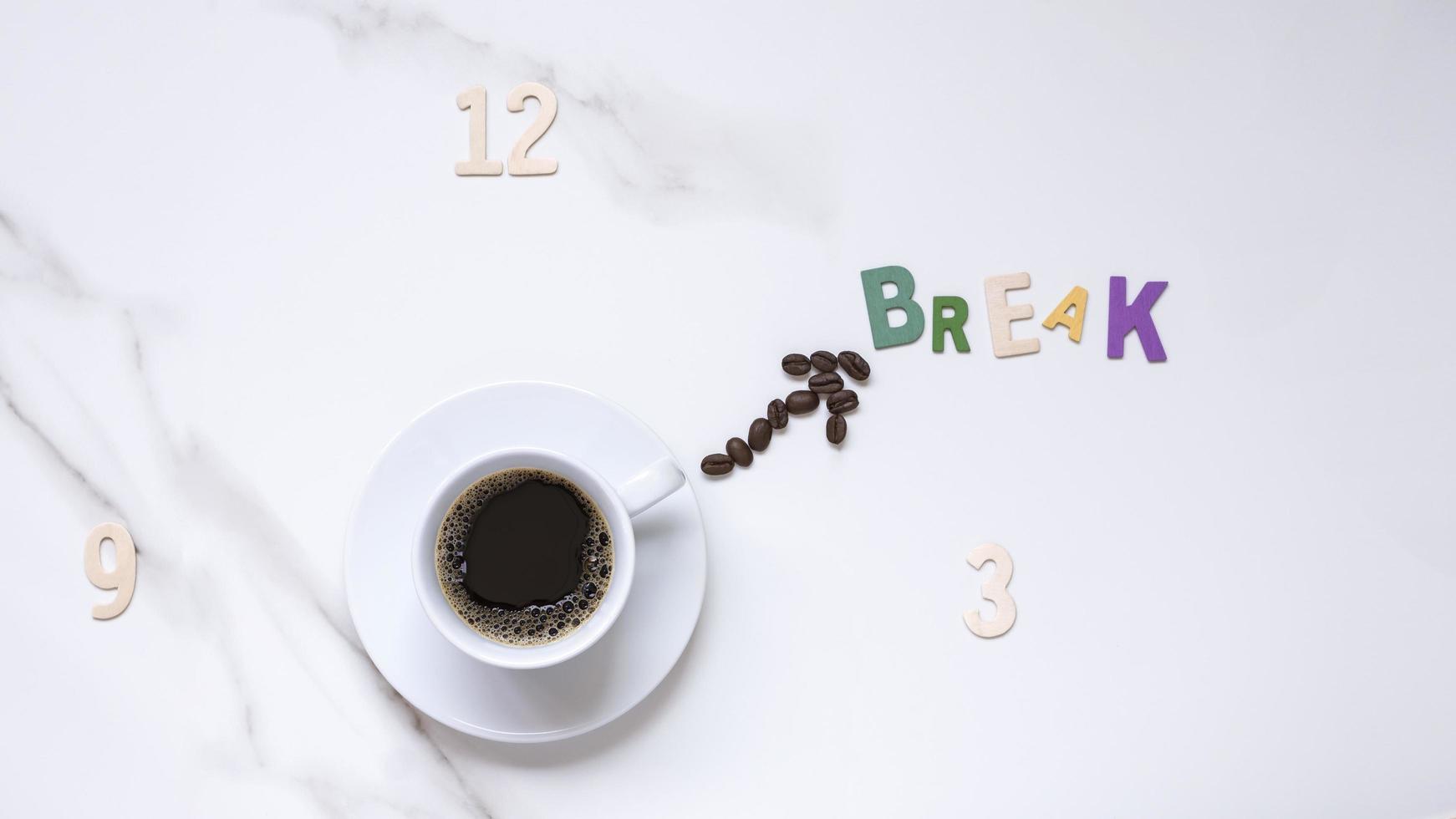 Top view of black coffee in white ceramic cup and coffee beans in clock hand shaped with wooden numbers and Break word in clock face forming on white marble tabletop photo