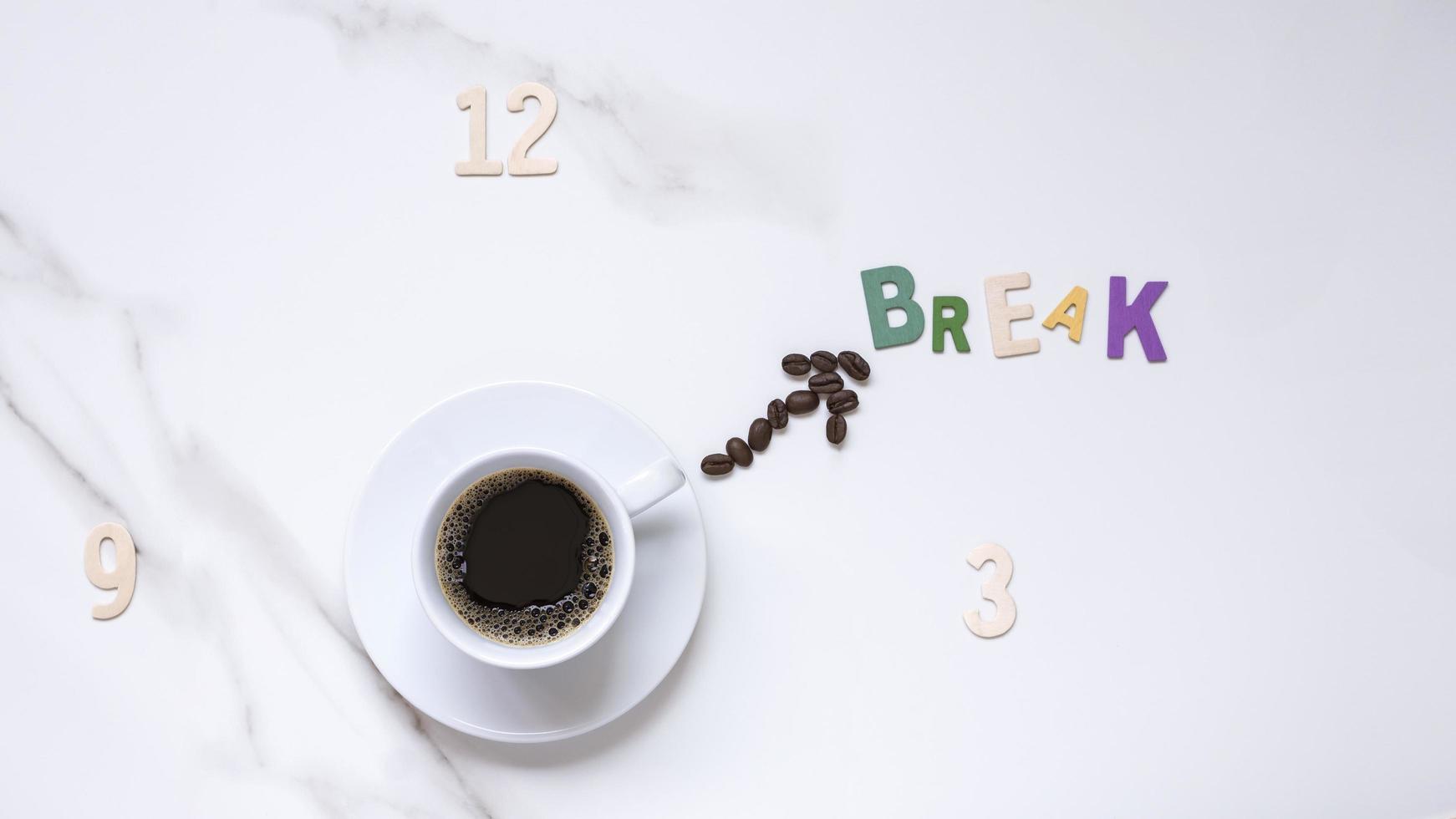 vista superior de café negro en una taza de cerámica blanca y granos de café en forma de mano de reloj con números de madera y palabra rota en la cara del reloj que se forma en una mesa de mármol blanco foto