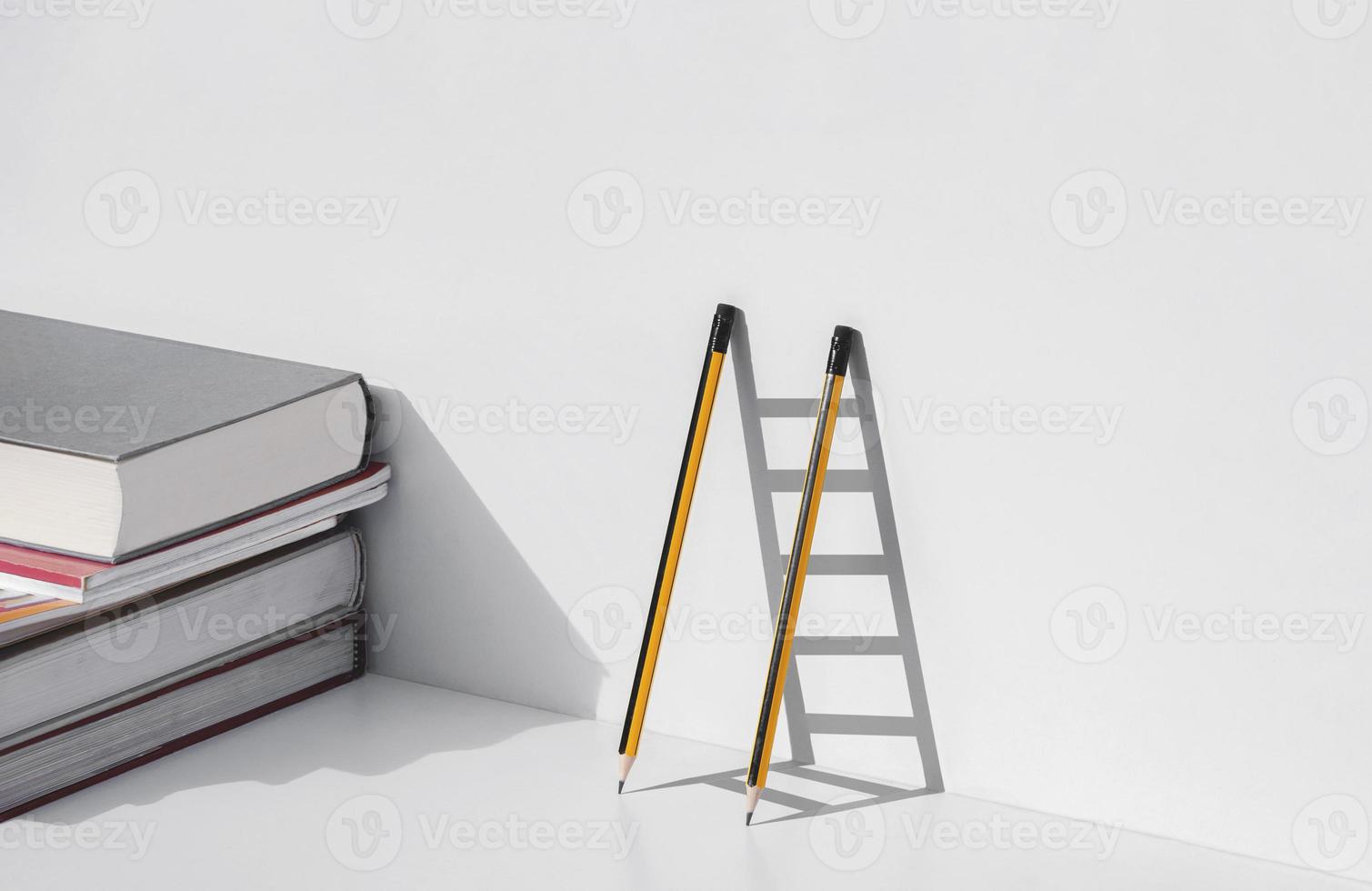 Two pencils and shadow in form of ladder with stack of textbooks on white tabletop, Education, learning is the ladder to success concept photo