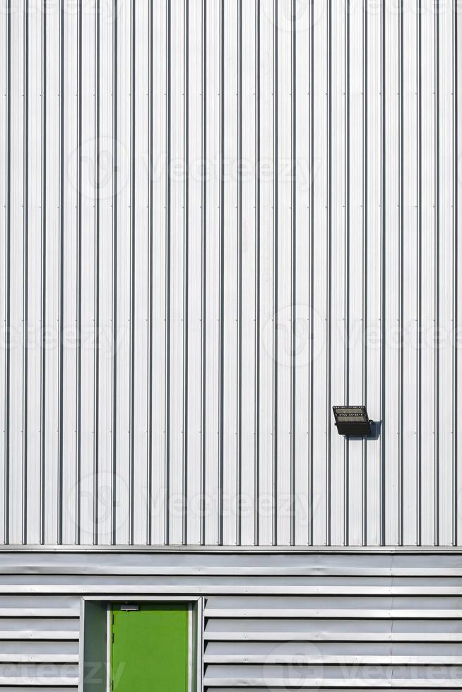 Front view of green steel door with LED spotlight solar cell on corrugated metal wall of large industrial building in minimal style and vertical frame photo