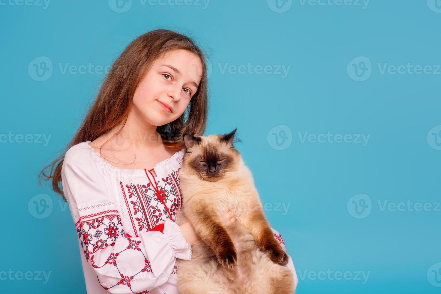 Teen girl with a cat Neva masquerade in her arms. Girl in the embroidered shirt on a blue background photo
