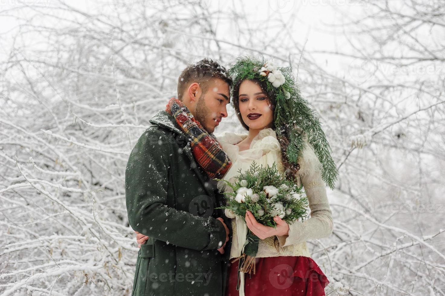 Beautiful bride and groom with a white dog are standing on the background of a snowy forest. photo