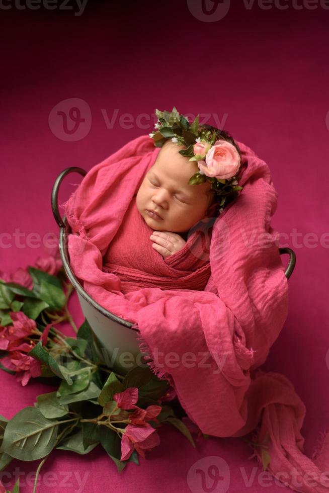 retrato de primer plano de una linda recién nacida durmiendo envuelta en una manta suave púrpura, usando una elegante flor de cabeza, concepto de moda para bebés foto