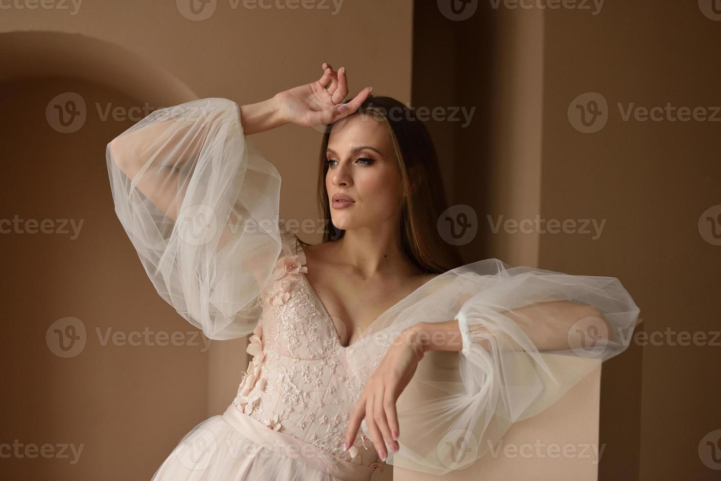 Portrait of a beautiful bride in full growth in the studio on a white background. The woman stands with her back and looks into the frame. photo