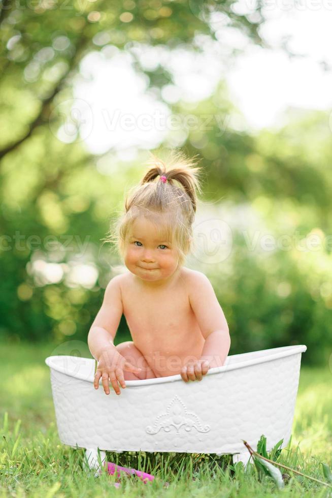 niña pequeña feliz toma un baño de leche con pétalos. niña en un baño de leche sobre un fondo verde. ramos de peonías rosas. bebe bañándose Higiene y cuidado de los niños pequeños. foto