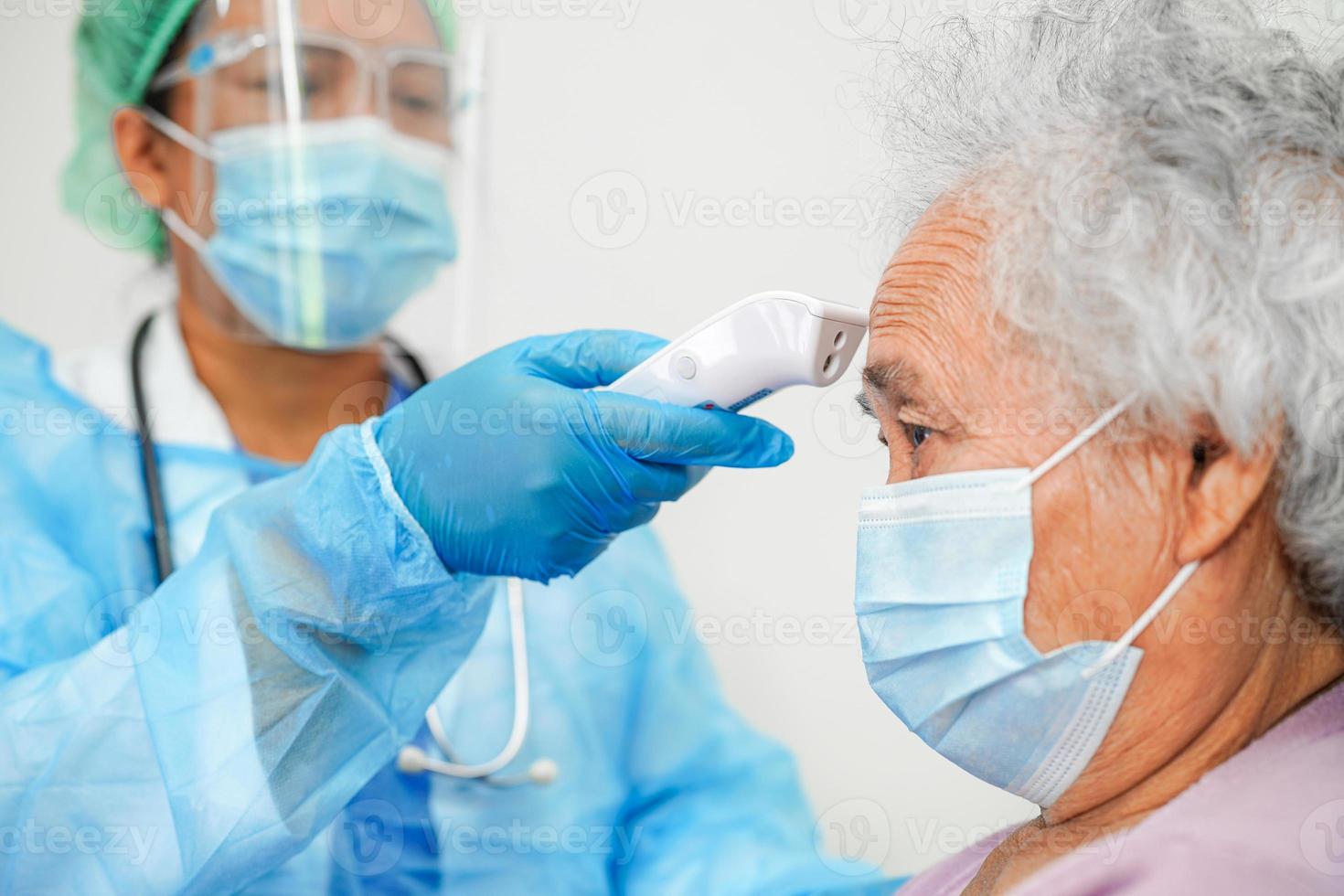 Doctor in ppe user infrared thermometer to check temperature of asian elderly woman patient for safety to protect covid 19 virus. photo