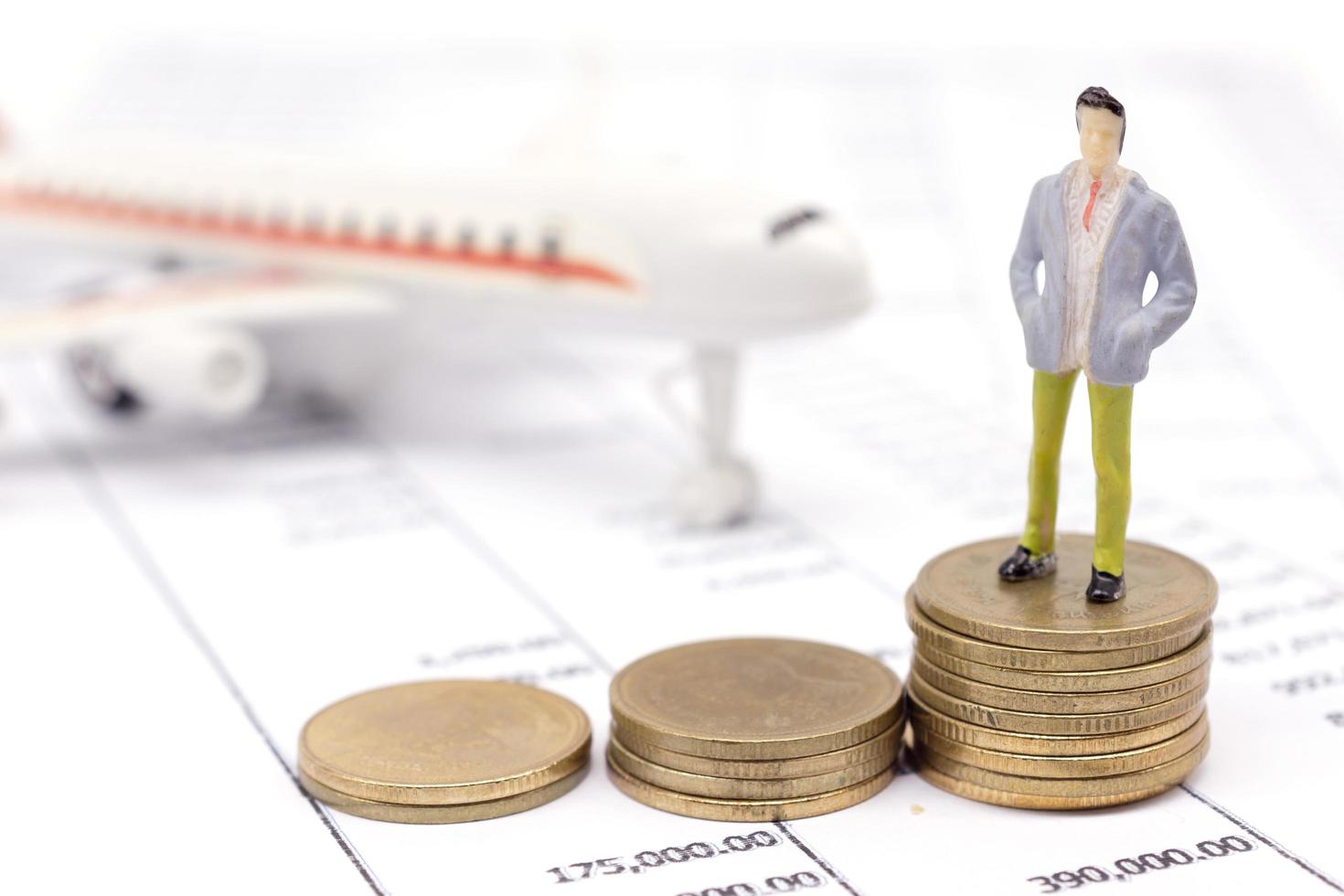 hombre de negocios en miniatura y pila de monedas en declaración y el avión detrás. concepto de ahorro y préstamo. foto