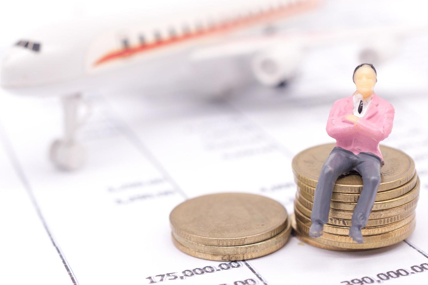 Miniature businessman and stack coins on statement and the airplane behind. saving and loan concept. photo