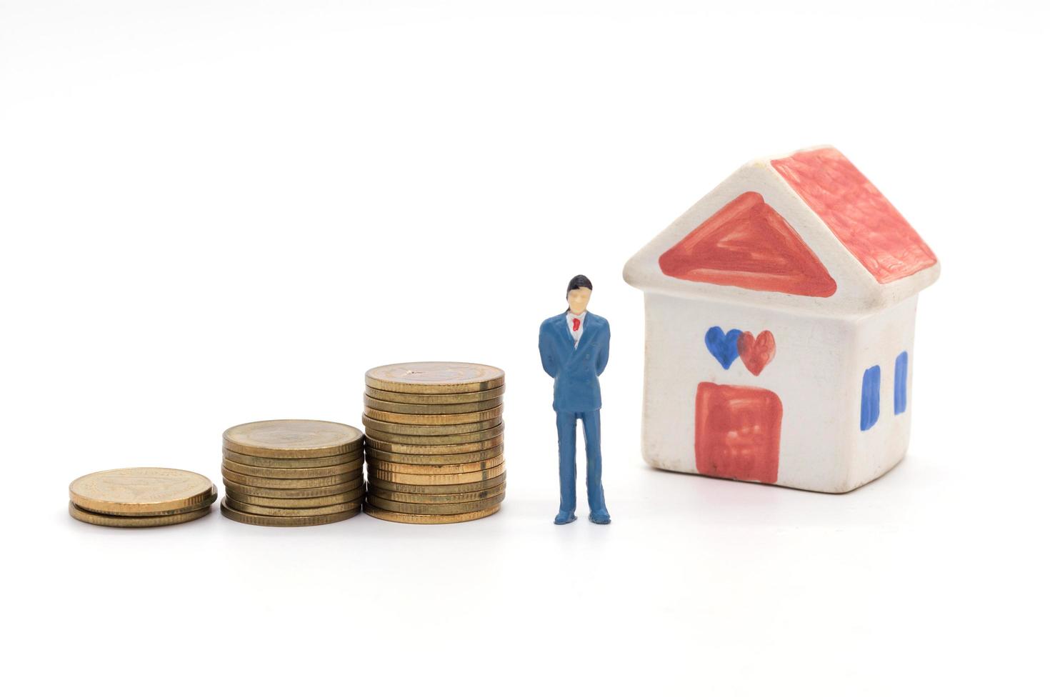 Miniature businessman standing on coins and the house behind. saving and loan concept. photo