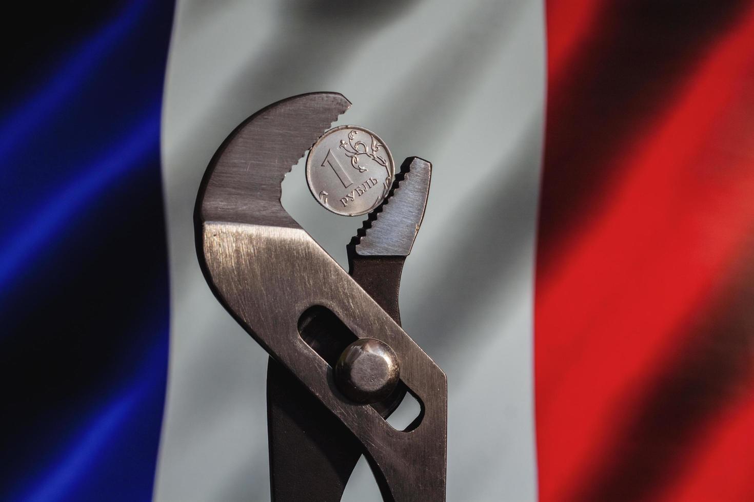 Coin one ruble is clamped in a wrench against the background of the flag of France. The idea of the collapse of the ruble and economy sanctions against Russia. photo