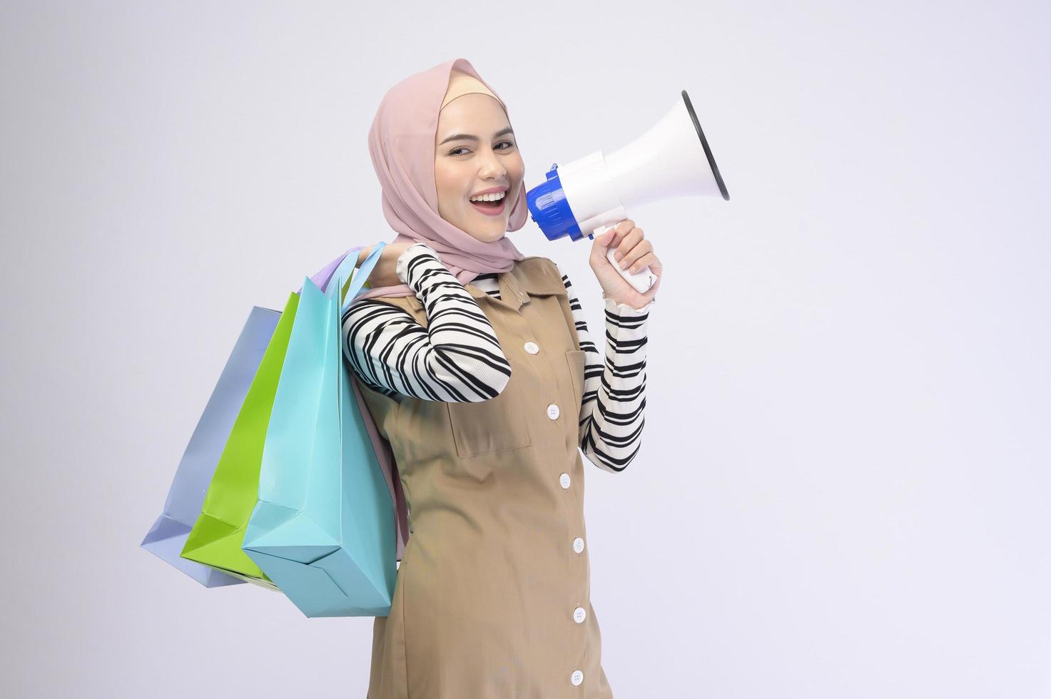 Young beautiful muslim woman in suit holding colorful shopping bags over white background studio photo