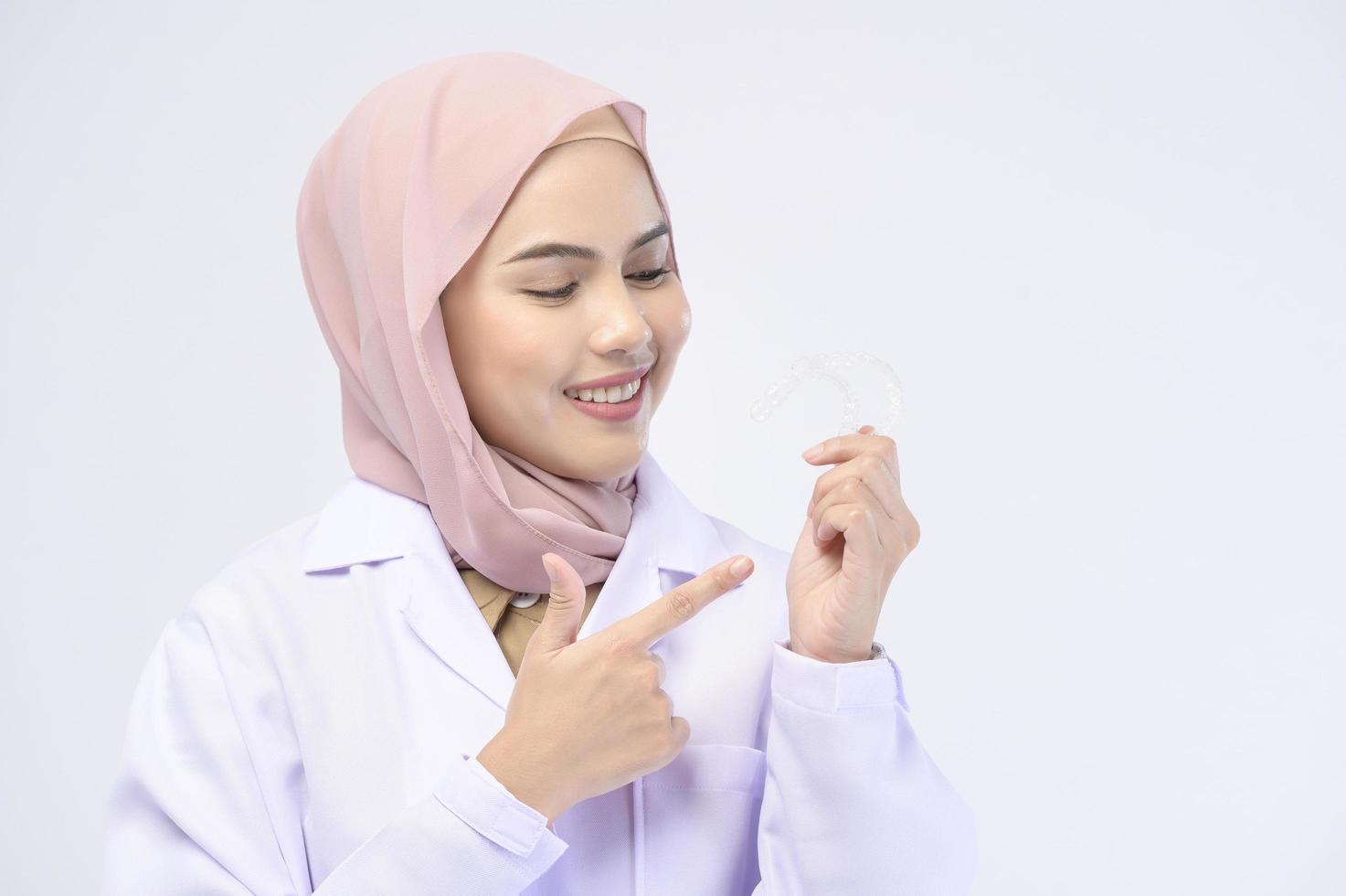 Muslim female dentist holding invisalign braces over white background studio, dental healthcare and Orthodontic concept. photo