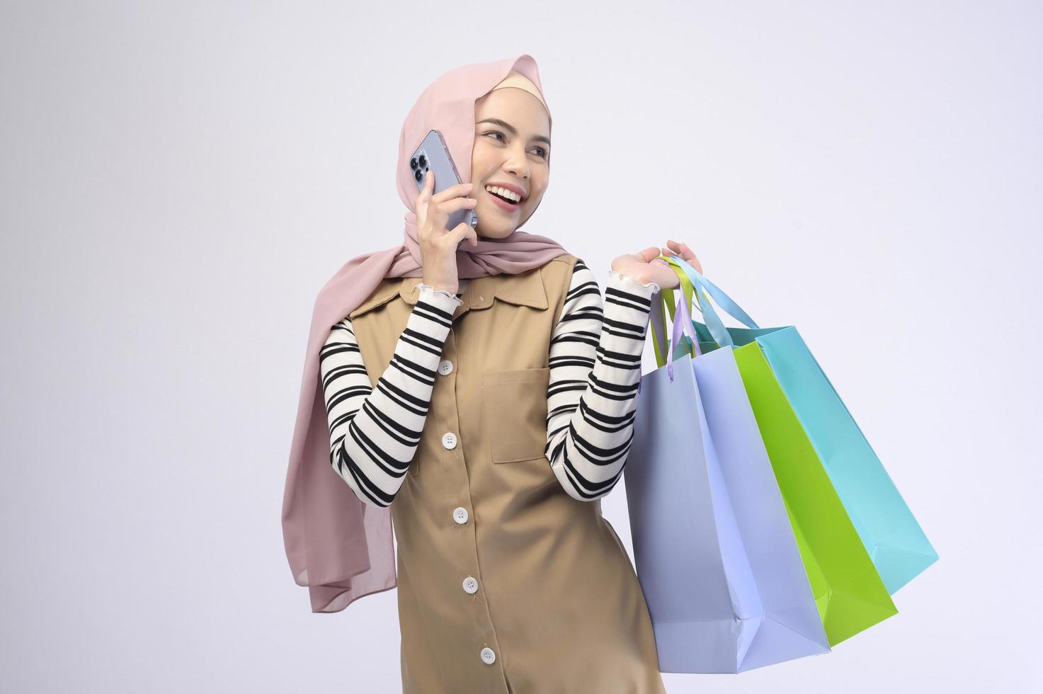 Young beautiful muslim woman in suit holding colorful shopping bags over white background studio photo