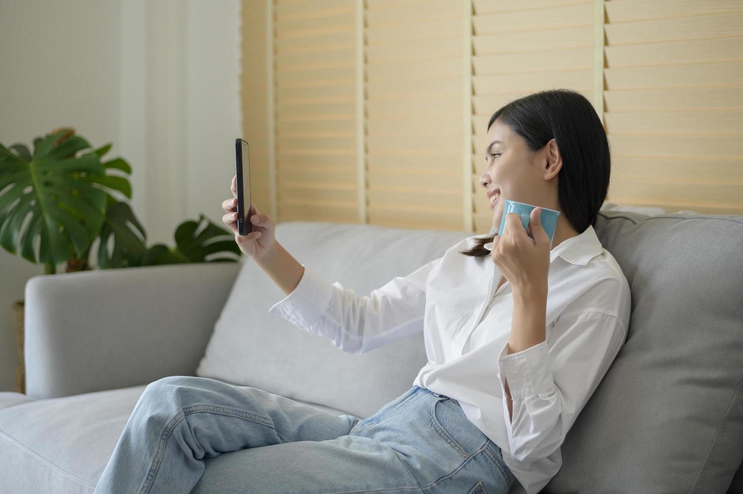 Young happy woman relaxing and using smart phone at home, social media and technology concept. photo