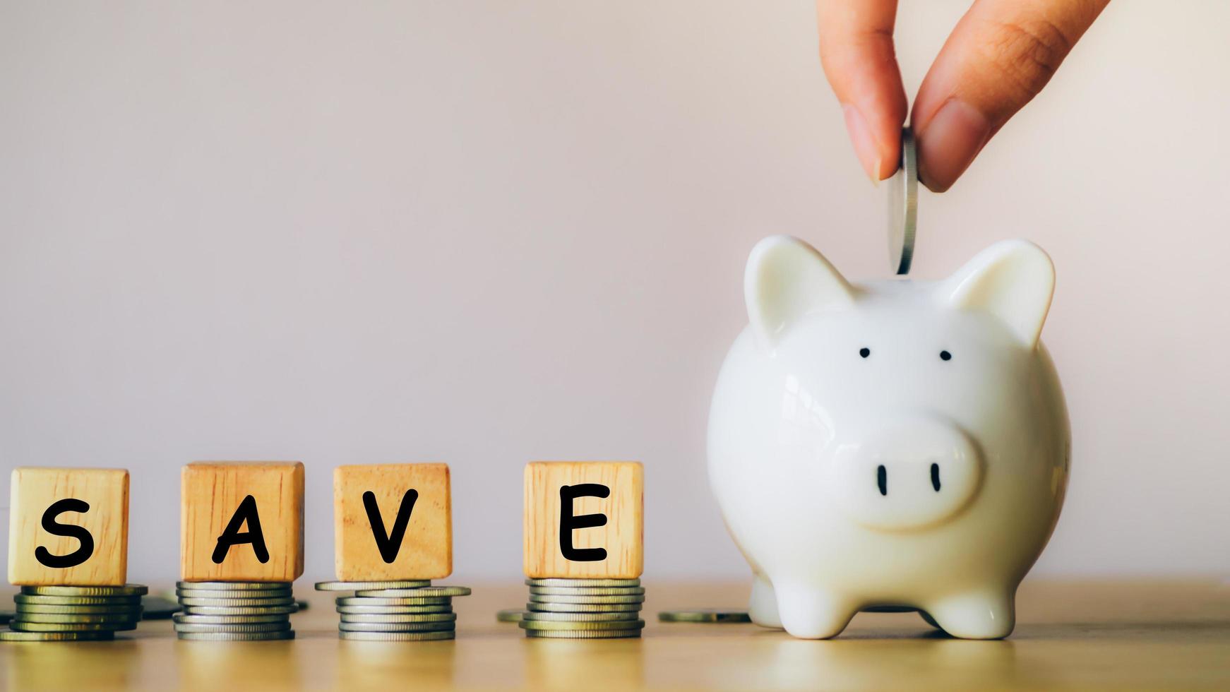 Hand of businessman is putting a coin into piggy bank near stack coins with the word save is written from a wooden block or cube. Loan, property ladder, financial, real estate investment concept. photo