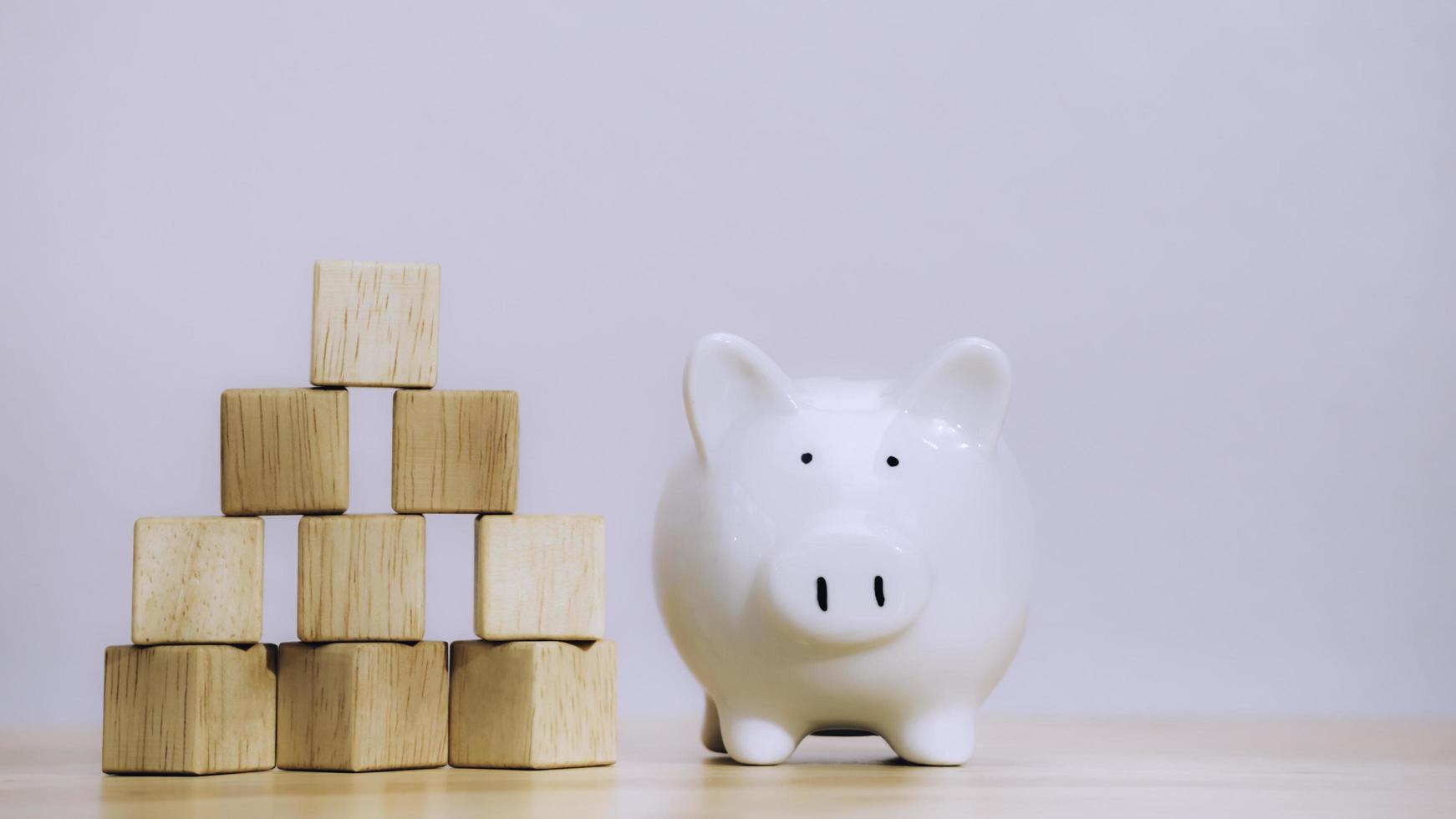 White piggy bank on stack coin near arranging wood cube with arrow symbol stacking as growth step stair on table to security of money invest for future. Growth successful and target concept. photo