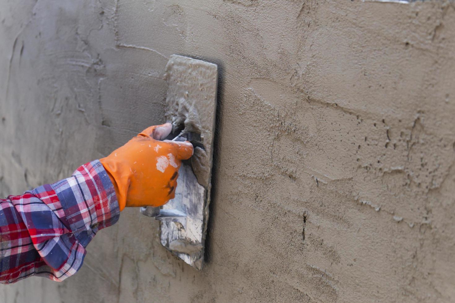 The hands of a worker who are plastering up close are wearing orange rubber gloves to prevent the cement from biting their hands, building the house wall photo