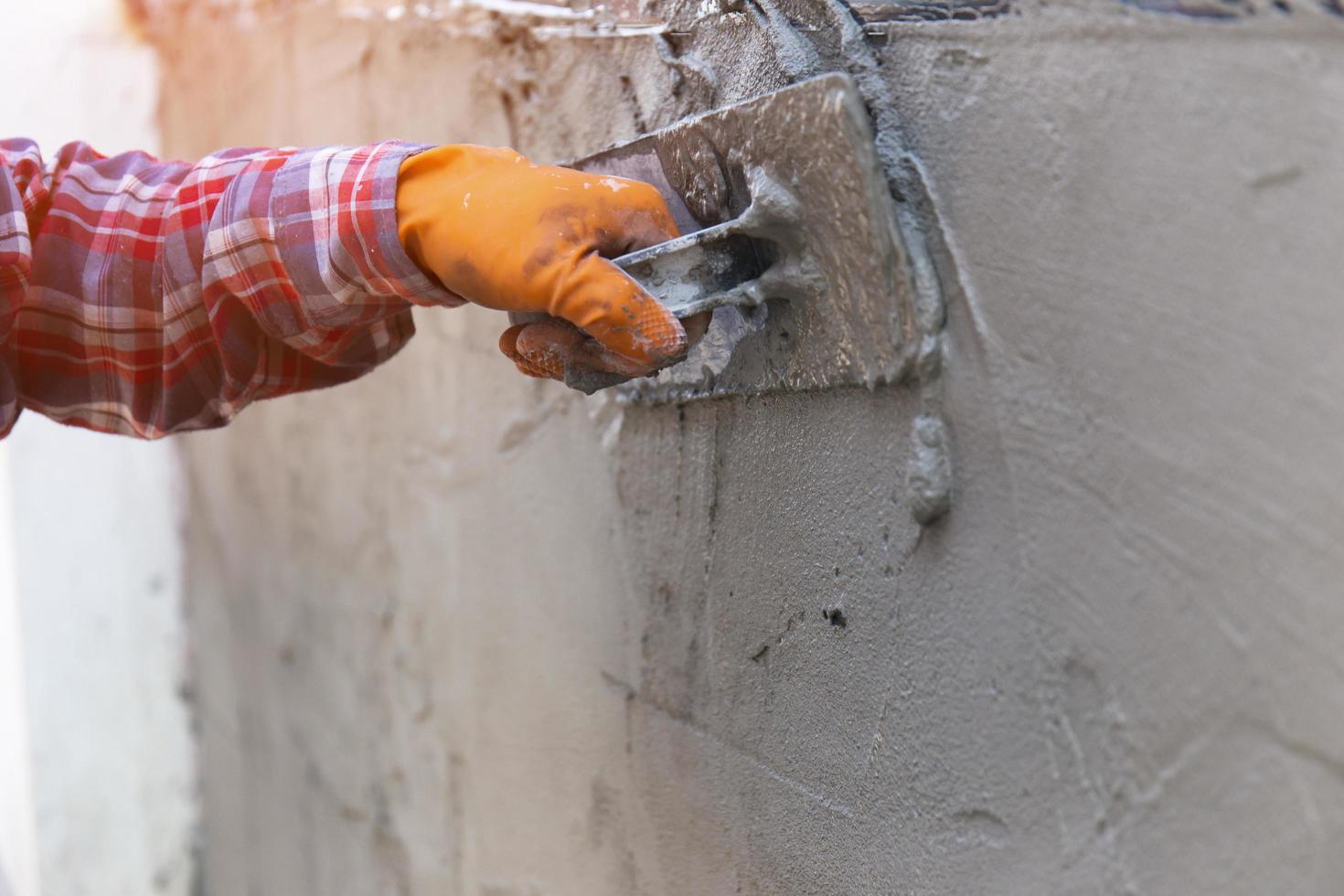 The hands of a worker who are plastering up close are wearing orange rubber gloves to prevent the cement from biting their hands, building the house walls and having beautiful orange lights. photo