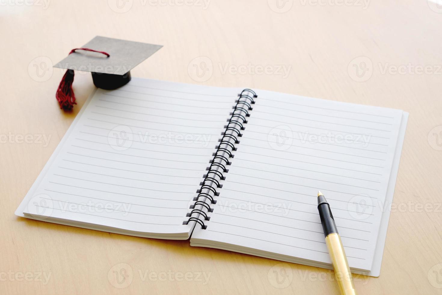 Blank notebook on the table and graduation cap photo