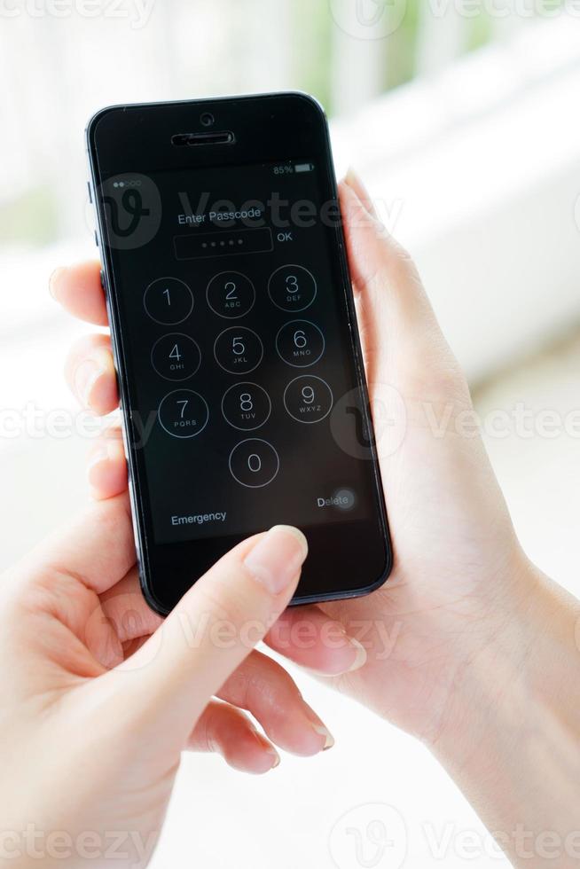 Young woman hand holding the Apple iPhone 5 and enter passcode. The cellular phone is produced by Apple Computer, Inc photo