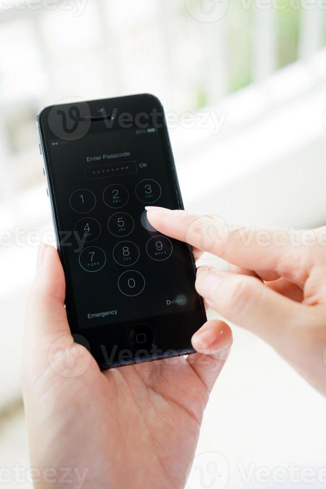 Young woman hand holding the Apple iPhone 5 and enter passcode. The cellular phone is produced by Apple Computer, Inc photo