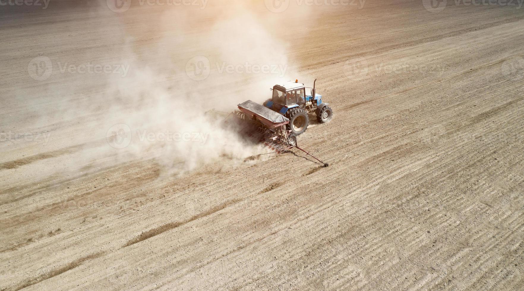 Aerial view of tractor with mounted seeder performing direct seeding of crops on plowed agricultural field. Farmer is using farming machinery for planting process, top view photo