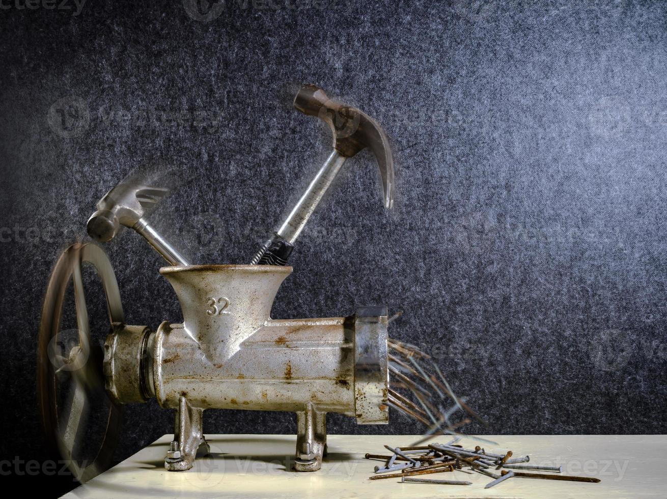 A Grinder crushing Hammers into Nails Creative Concept photo