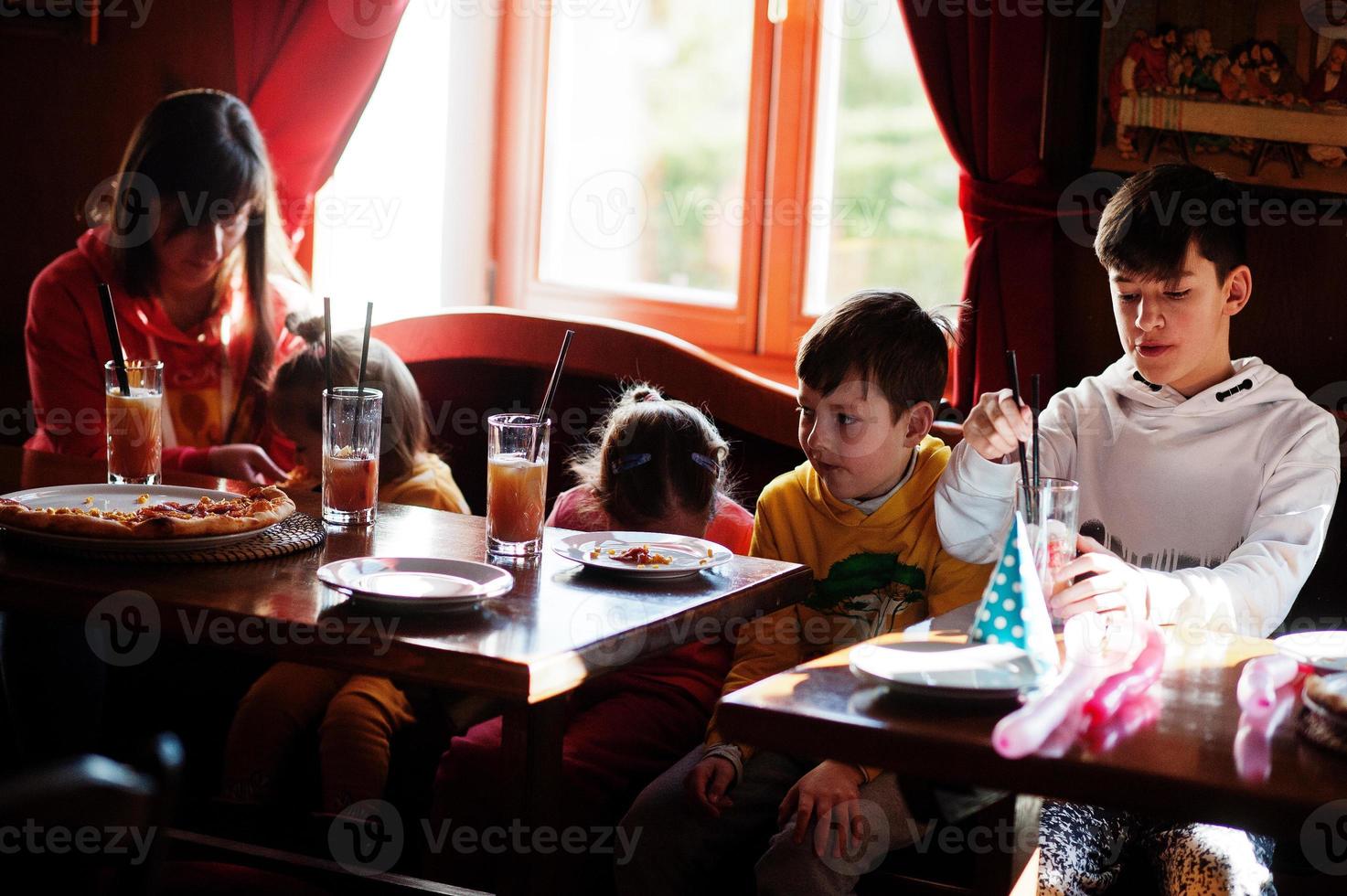 niños en cumpleaños sentados en la mesa y comiendo pizza. foto