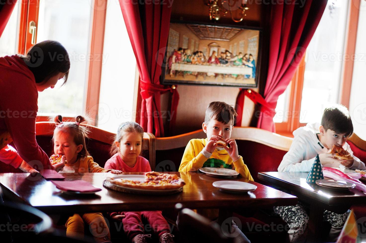 niños en cumpleaños sentados en la mesa y comiendo pizza. foto