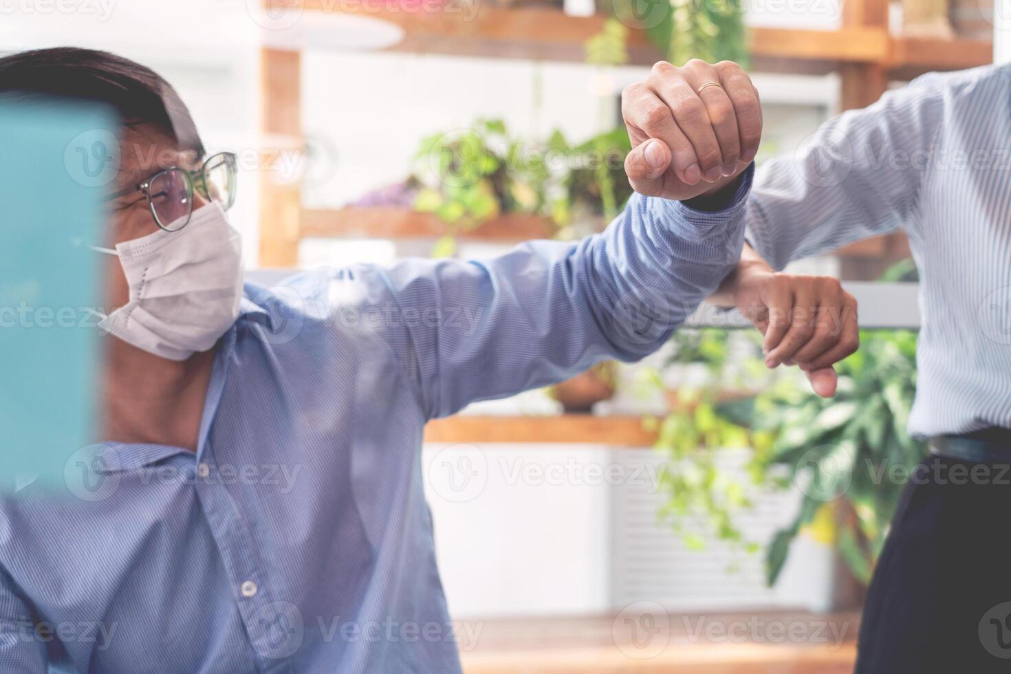 Two Asian colleagues in medical masks avoid a handshake when meeting in the office greeting with bumping elbows during coronavirus COVID-19 epidemic in office, Social distancing concept. photo