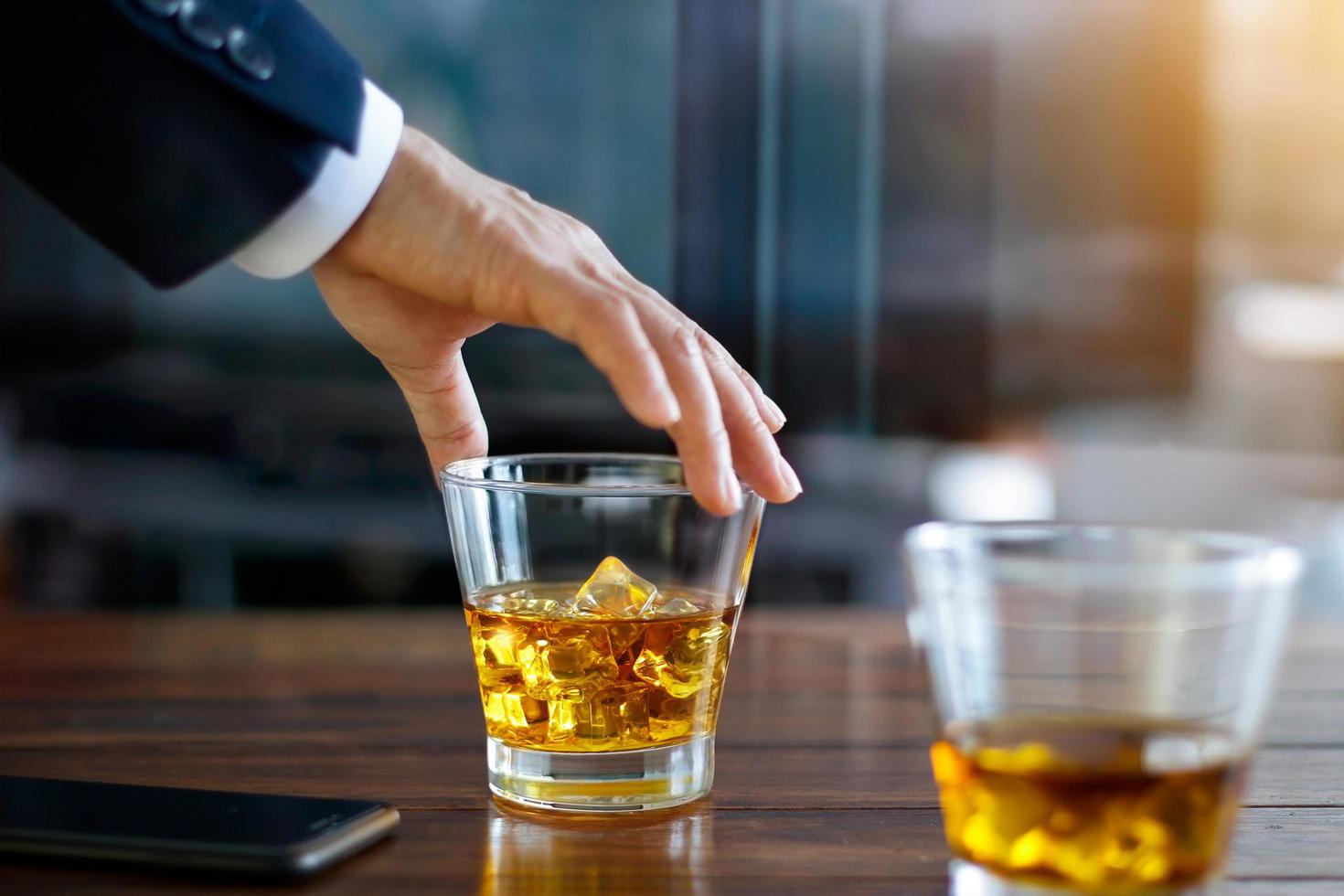 Hand of businessman touching glass of bourbon whiskey in building background photo