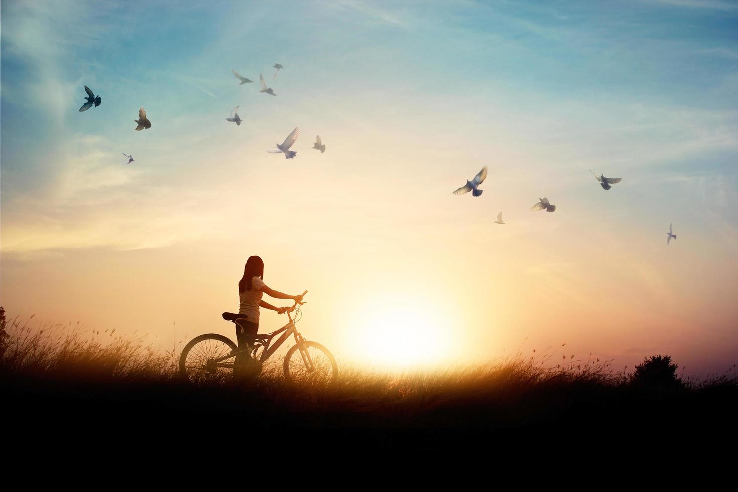 mujer solitaria parada con bicicleta en el camino del campo de arroz entre pájaros voladores y fondo de puesta de sol foto