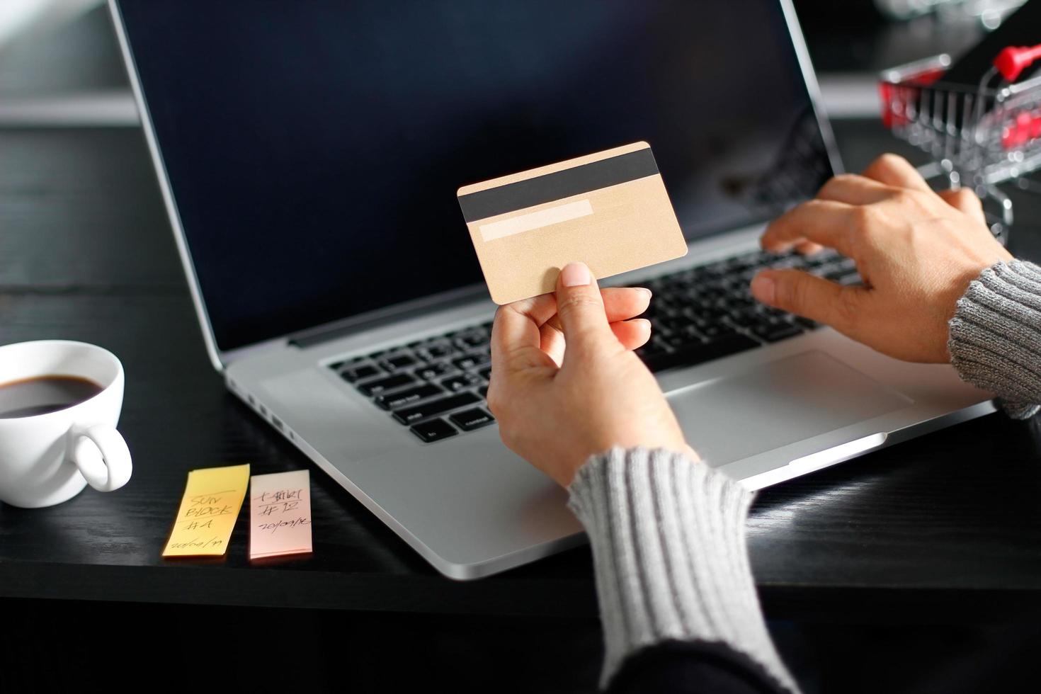 concepto de compras en línea. mujer con tarjeta de crédito dorada en la mano y compras en línea usando una computadora portátil en casa. foto