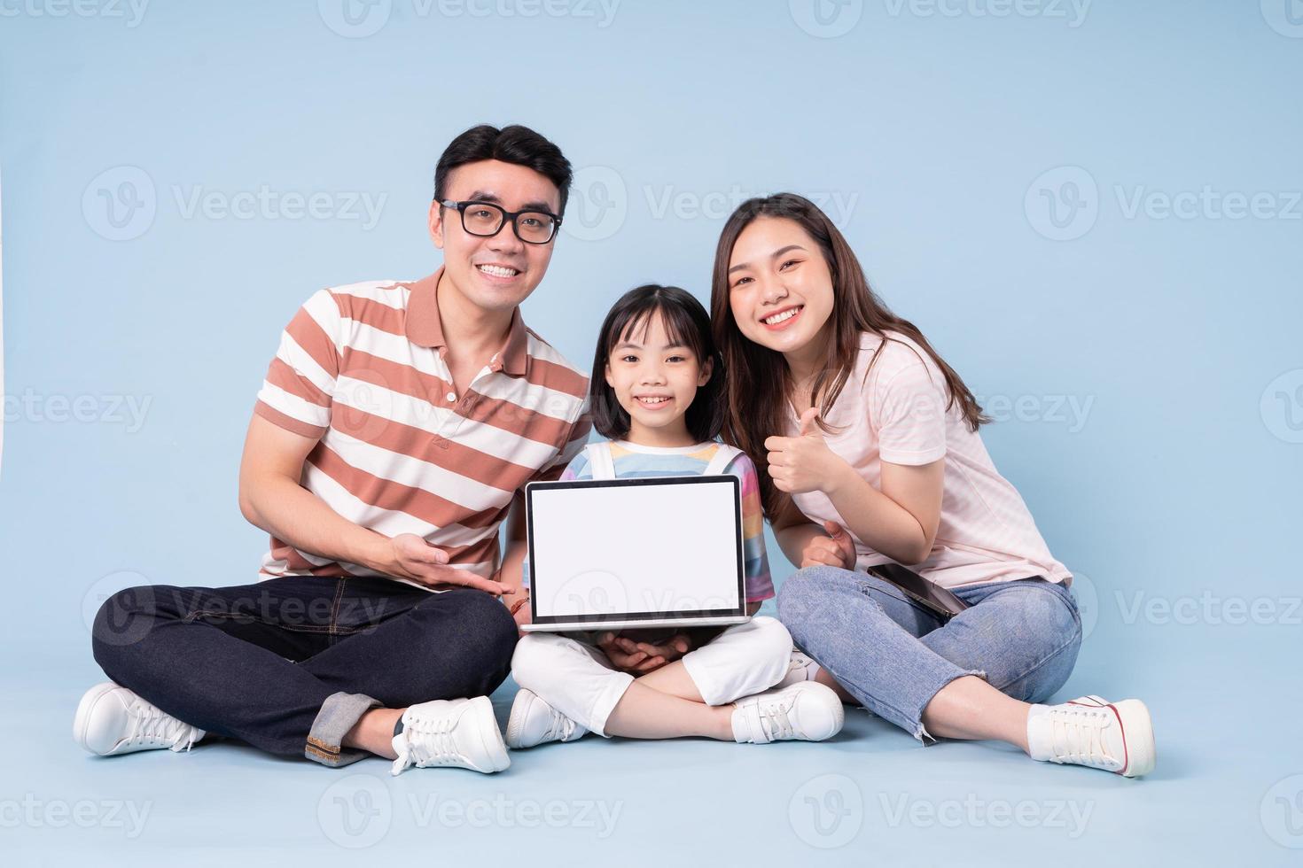 imagen de una joven familia asiática usando una laptop con fondo azul foto