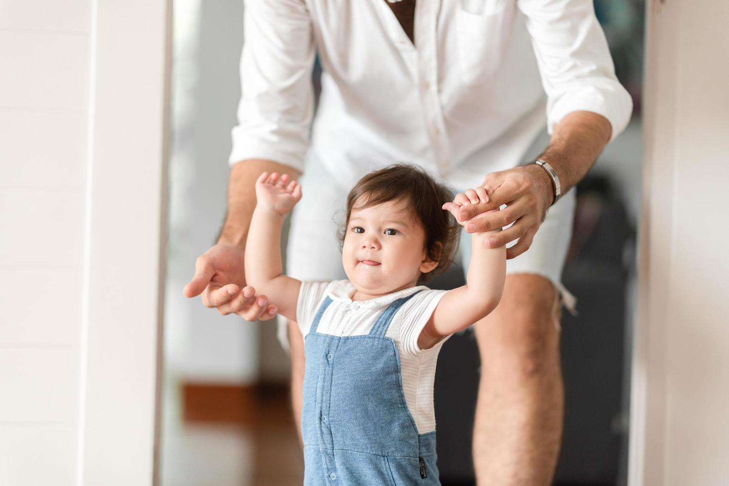 lindo concepto de familia de niño pequeño, bebé aprendiendo a caminar con el padre y la madre para ayudar a cuidar y tomar la mano, primer paso con el apoyo de los padres de la infancia, pequeño retrato de amor niño pequeño en casa foto