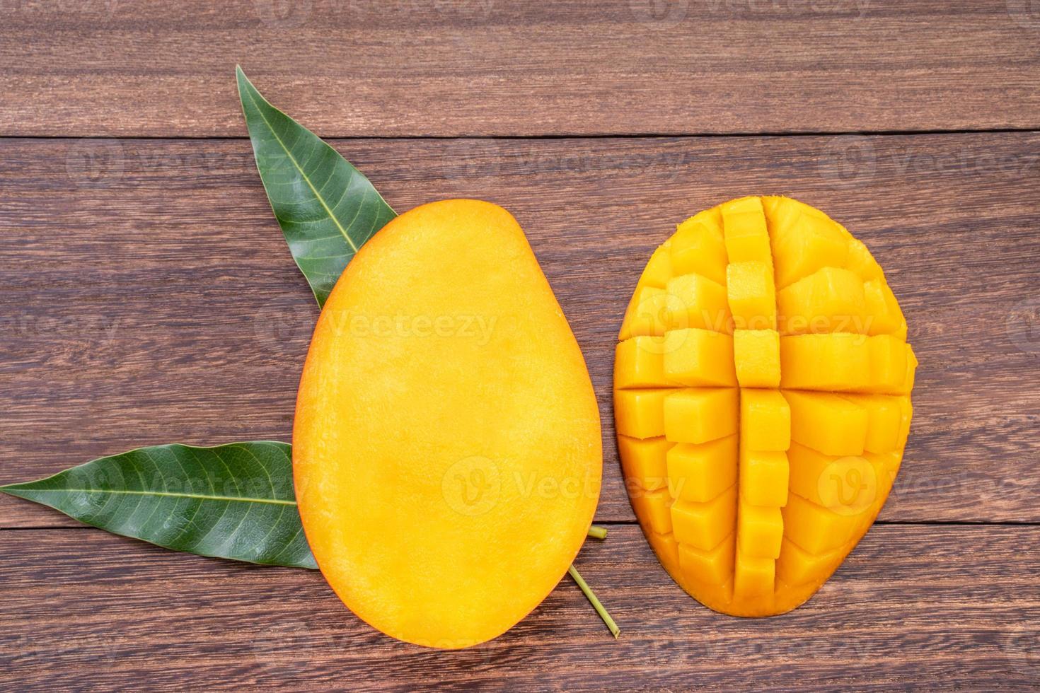 Fresh mango - beautiful chopped fruit with green leaves on dark wood background. Tropical fruit design concept. Flat lay. Top view. Copy space. photo