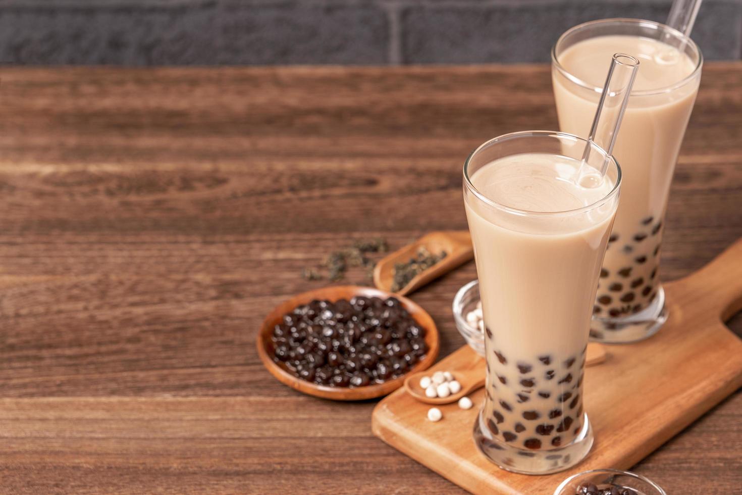 Popular Taiwan drink - Bubble milk tea with tapioca pearl ball in drinking glass and straw, wooden table gray brick background, close up, copy space photo