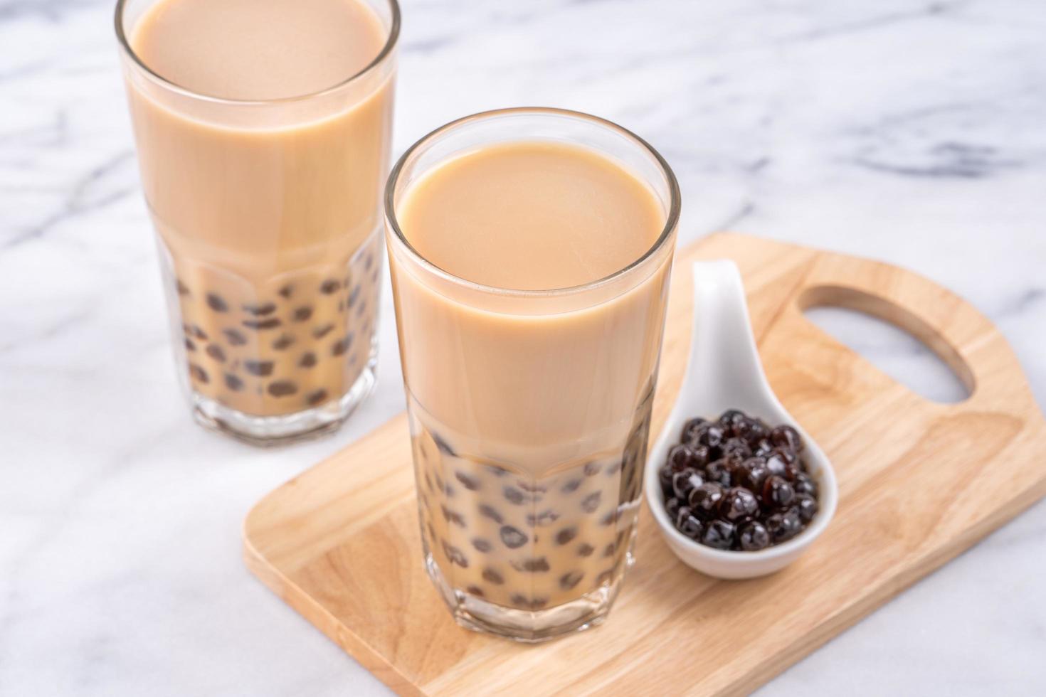 Popular Taiwan drink - Bubble milk tea with tapioca pearl ball in drinking glass on marble white table wooden tray background, close up, copy space photo