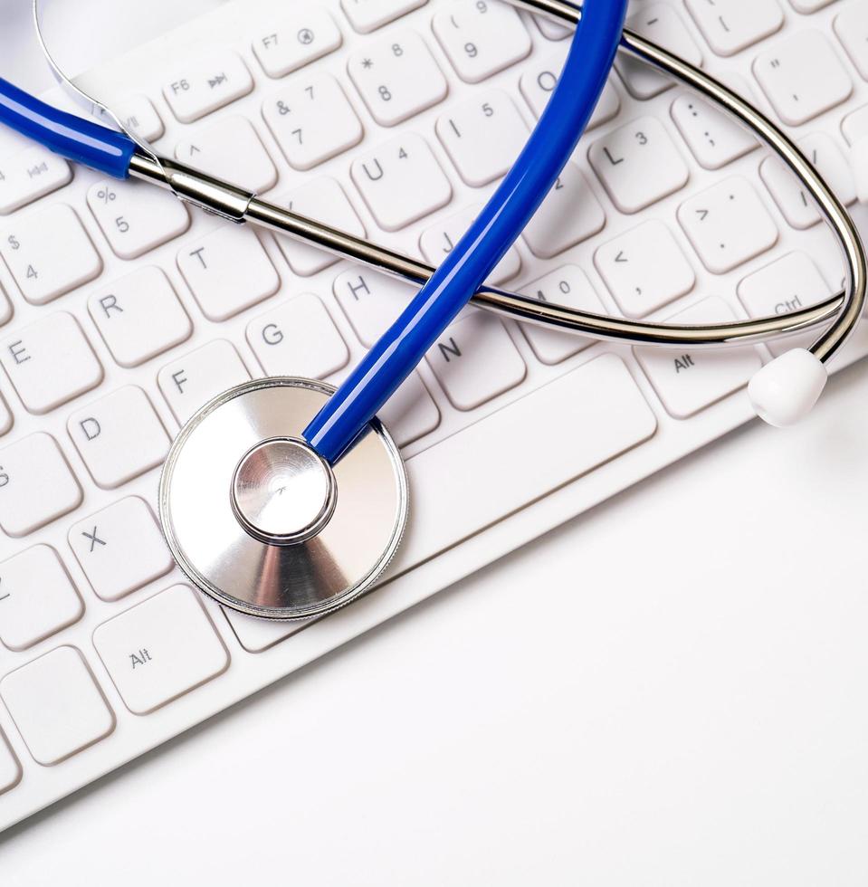 Blue stethoscope on computer keyboard on white table background. Online medical information treatment technology concept, close up, macro, copy space photo