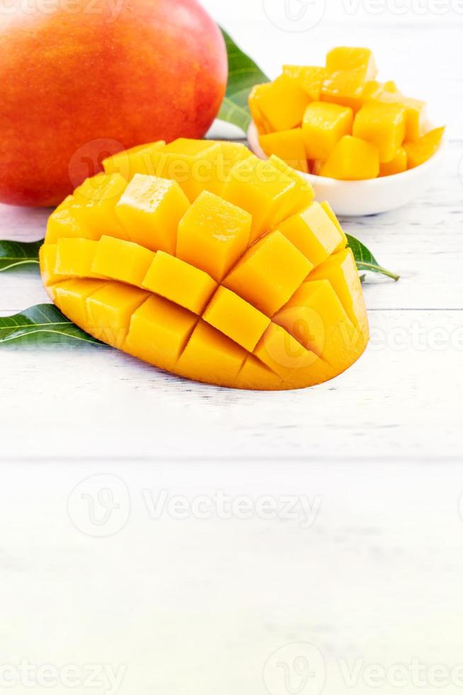 Beautiful chopped mango with green leaves on bright white color timber background. Above Top view, flat lay, copy space, close up. Tropical fruit concept. photo