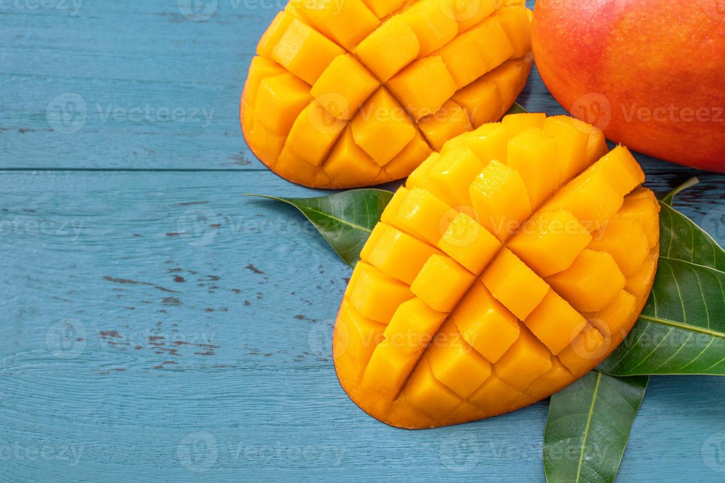 Fresh mango - beautiful chopped fruit with green leaves on dark blue timber background. Tropical fruit design concept. Flat lay. Top view. Copy space photo