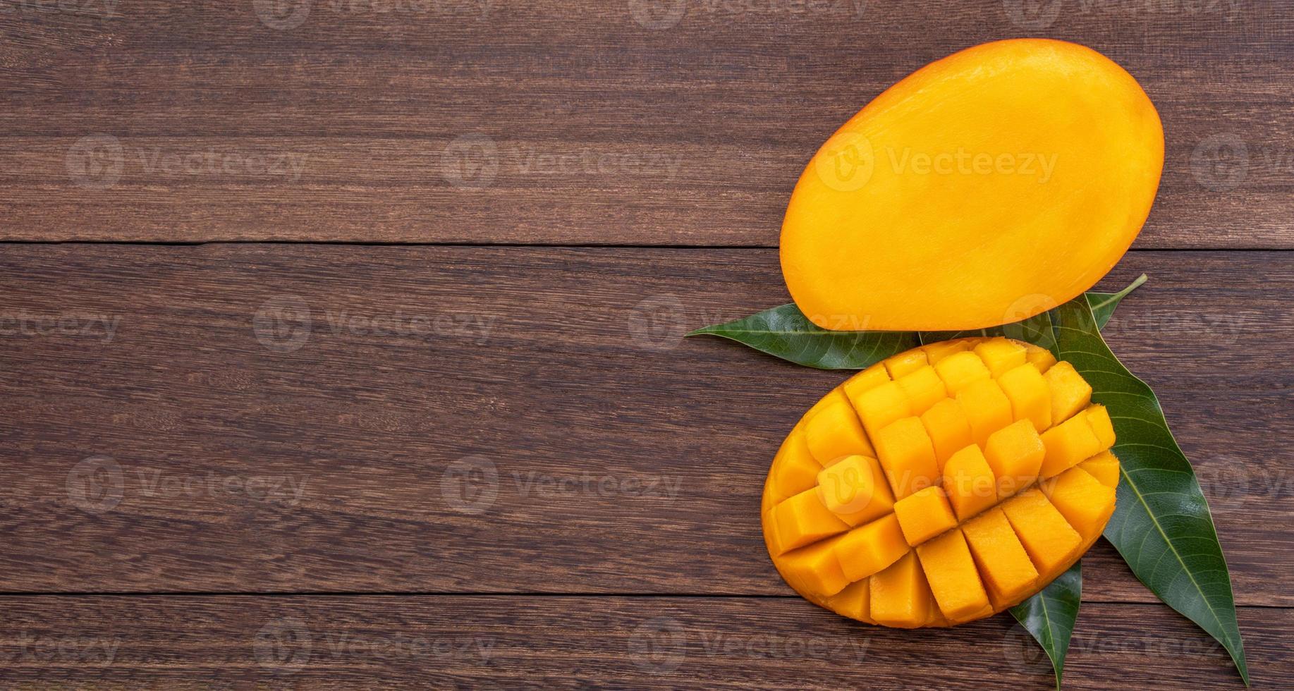 Fresh mango - beautiful chopped fruit with green leaves on dark wooden timber background. Tropical fruit design concept. Flat lay. Top view. Copy space photo