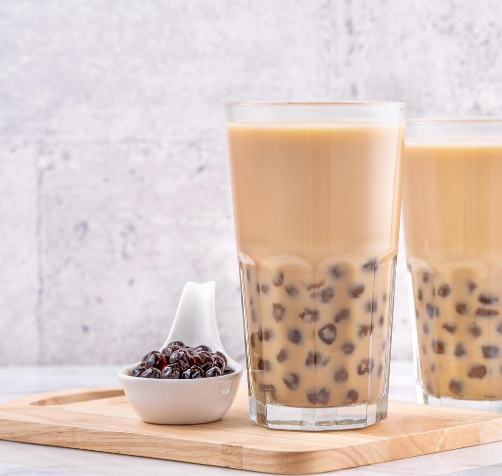 Popular Taiwan drink - Bubble milk tea with tapioca pearl ball in drinking glass on marble white table wooden tray background, close up, copy space photo
