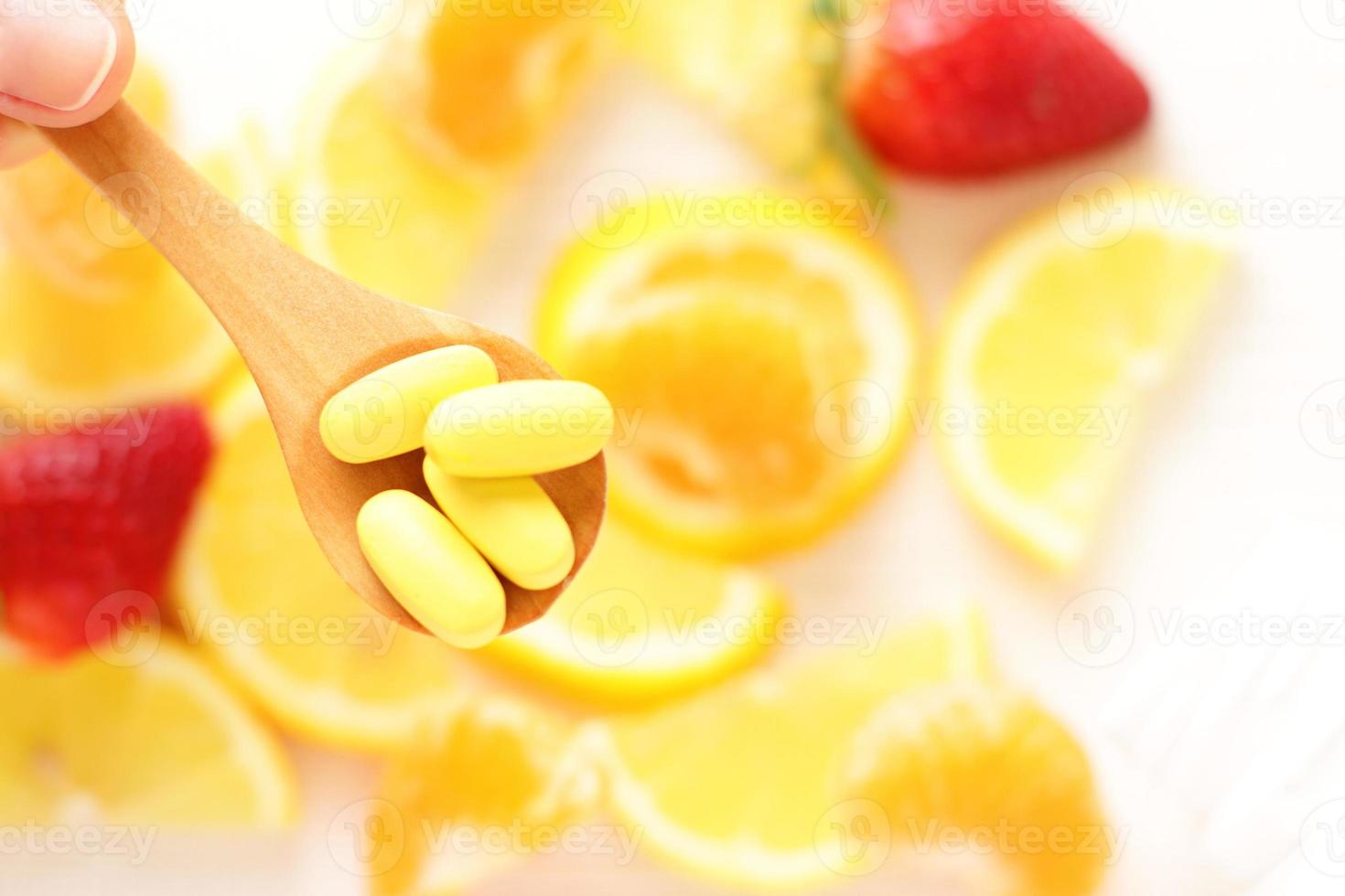 Vitamins pills on wooden spoon with lemon, orange, raspberry on background photo