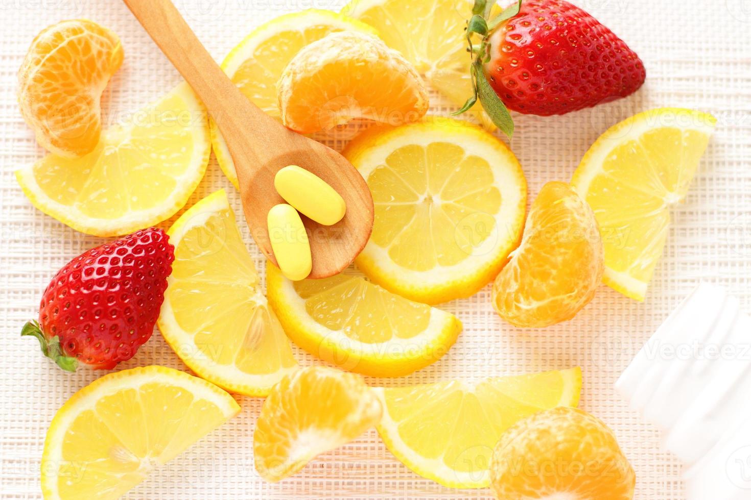 Vitamins pills on wooden spoon with lemon, orange, raspberry on background photo