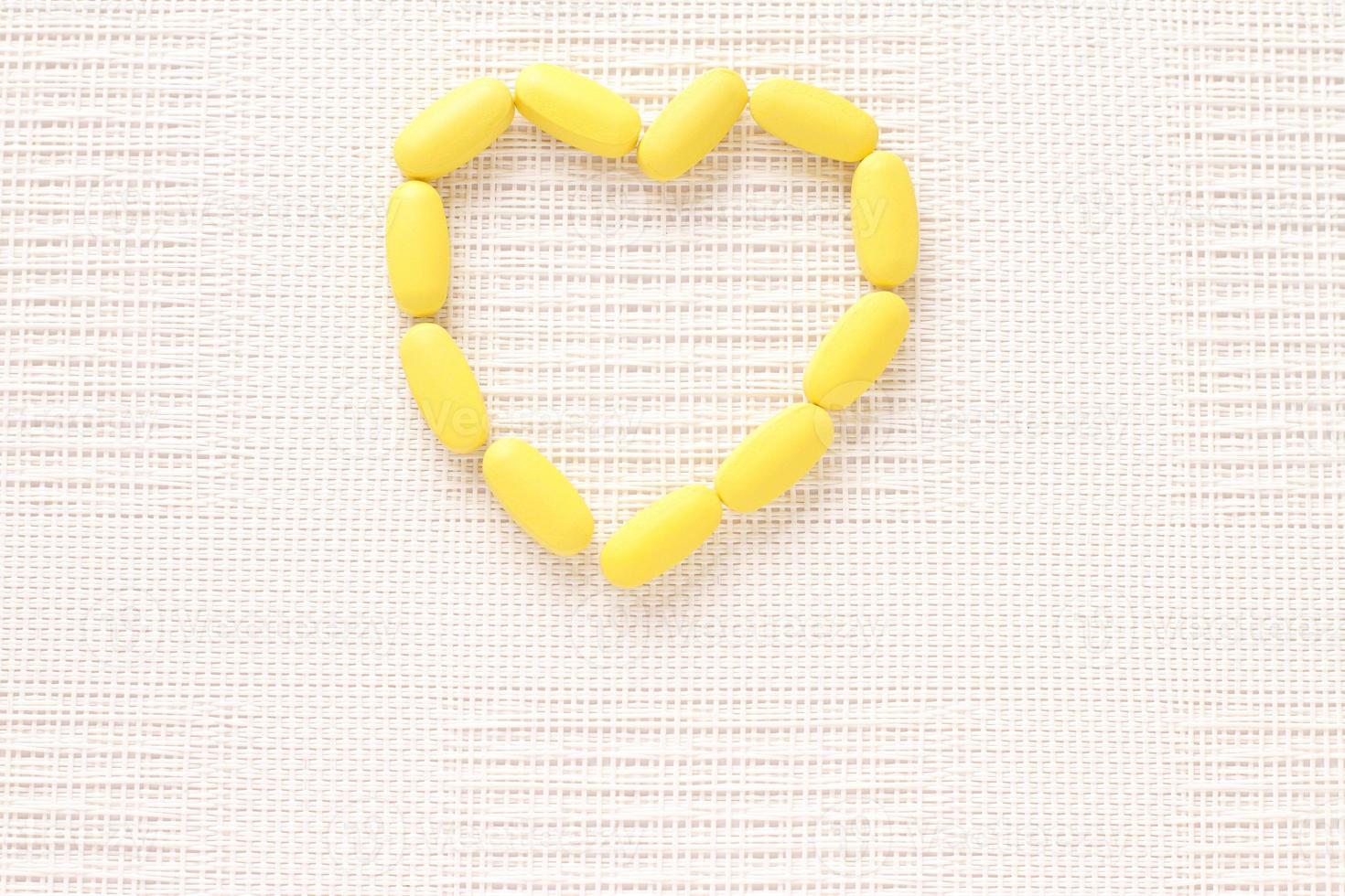 Vitamins pills on shape of heart, yellow tablets on table photo