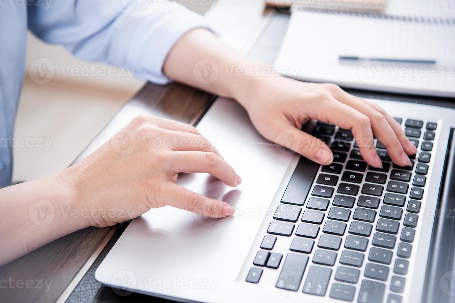 Business concept. Woman in blue shirt typing on computer with coffee on office table, backlighting, sun glare effect, close up, side view, copy space photo