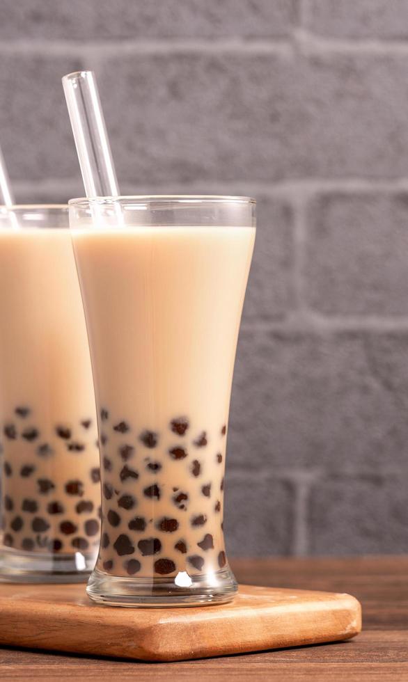 Popular Taiwan drink - Bubble milk tea with tapioca pearl ball in drinking glass and straw, wooden table gray brick background, close up, copy space photo
