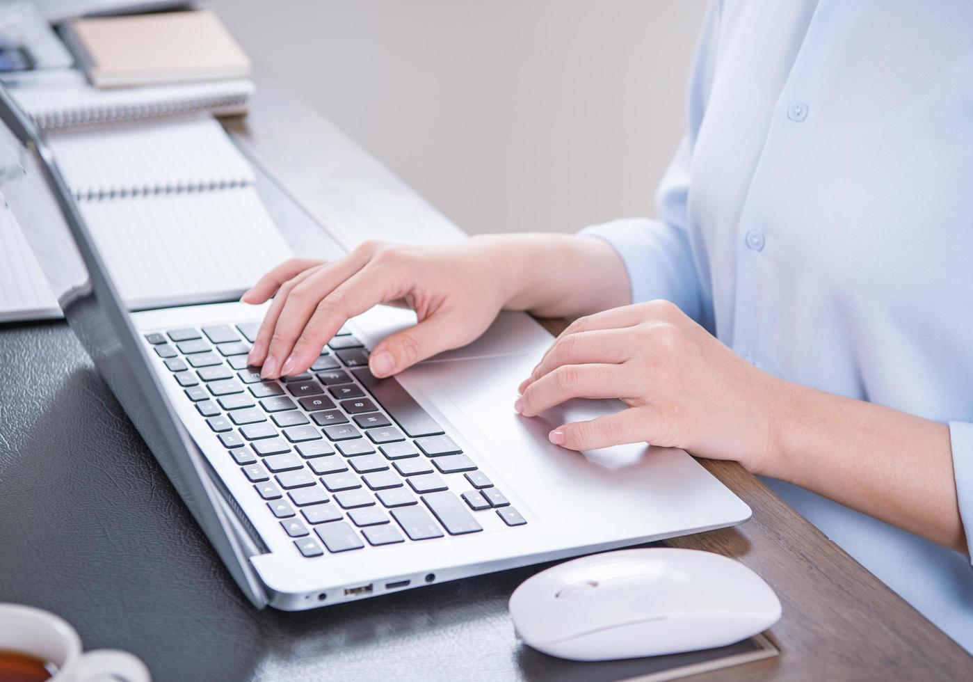 Business concept. Woman in blue shirt typing on computer with coffee on office table, backlighting, sun glare effect, close up, side view, copy space photo