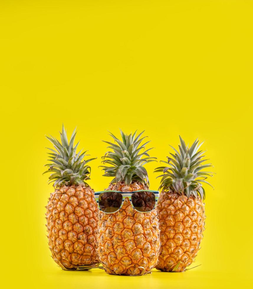 Creative pineapples with sunglasses isolated on yellow background, summer vacation beach idea design pattern, copy space, close up, blank for text photo